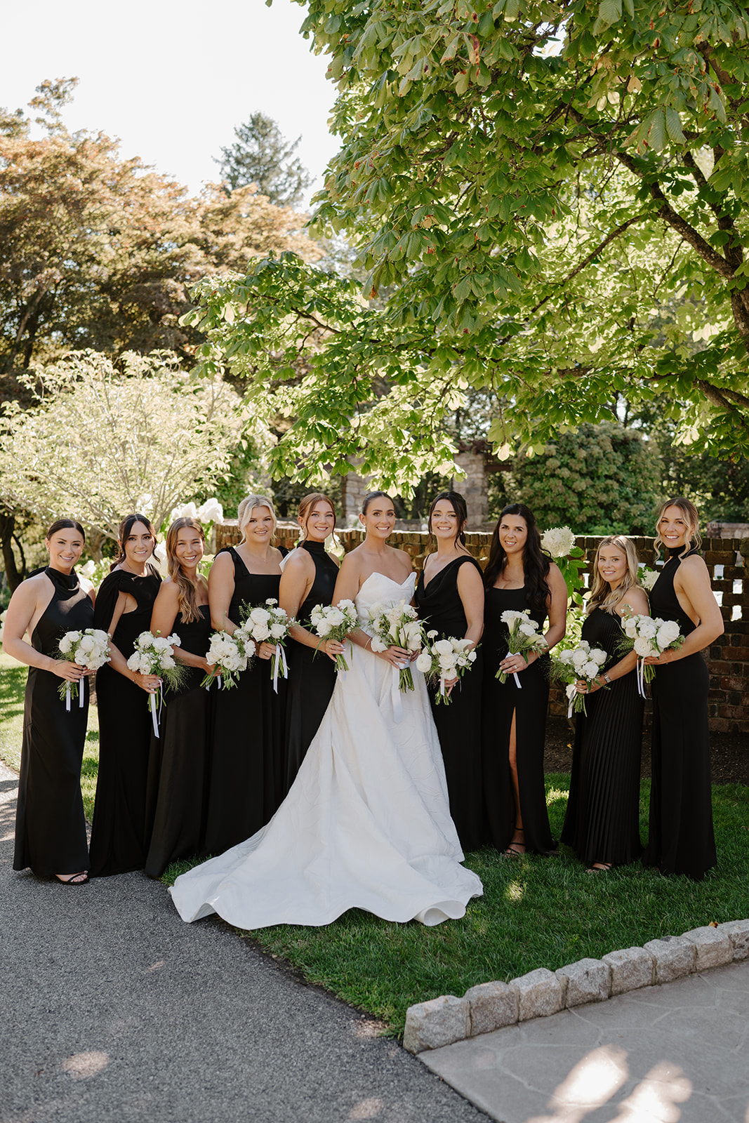 Bride standing with her bridesmaids in elegant black dresses holding matching white bouquets.